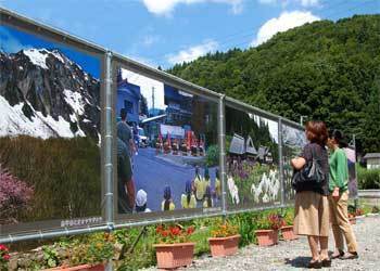 青空の下に展示された大型写真とそれに見入る観光客の写真